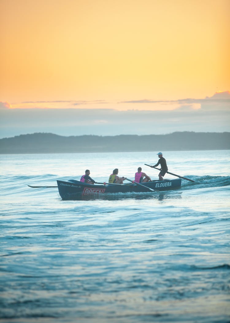 People Rowing On Boat At Sunset