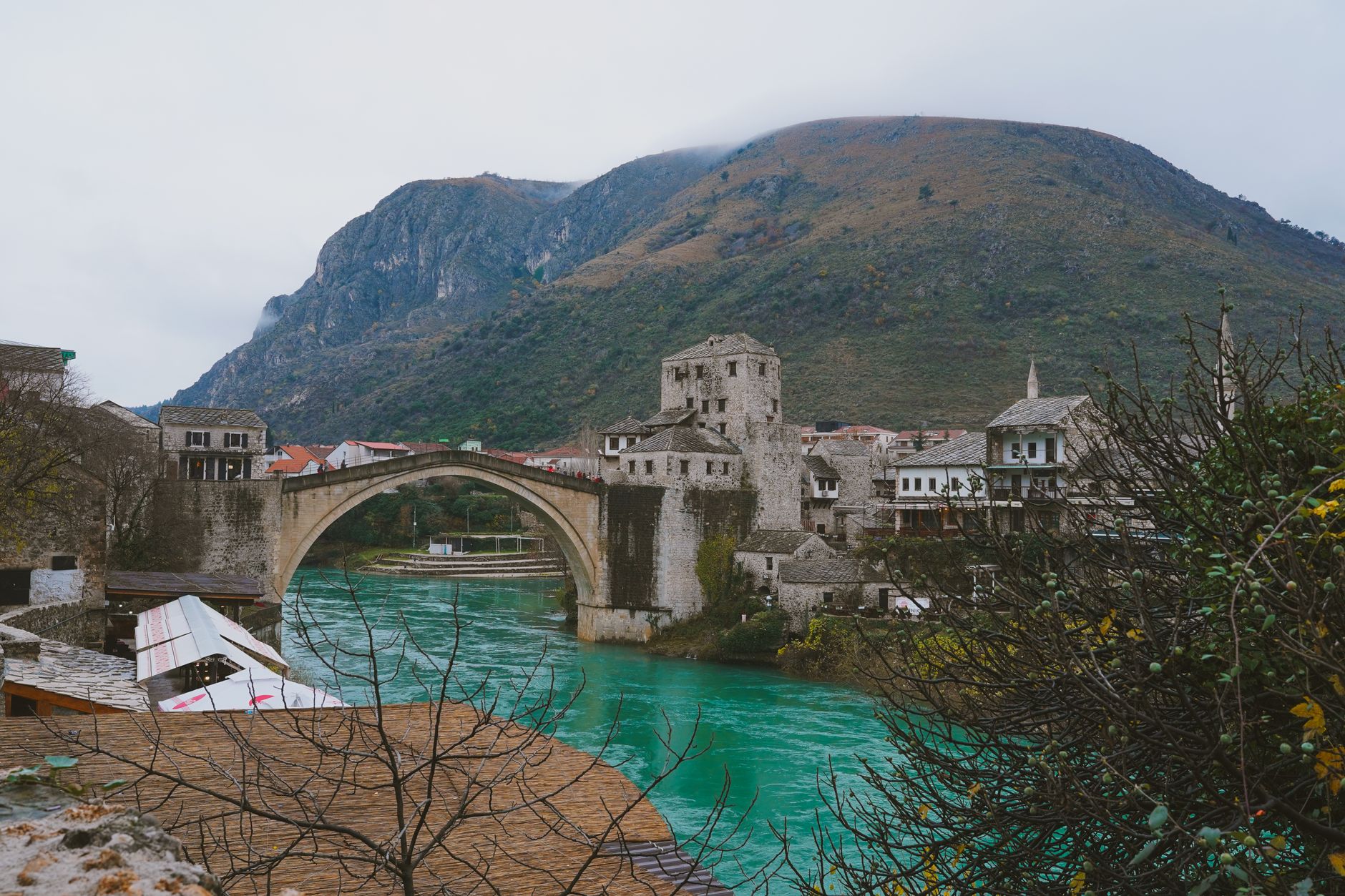 Scenic view of Mostar's famous Old Bridge over the emerald Neretva River, surrounded by historic buildings.