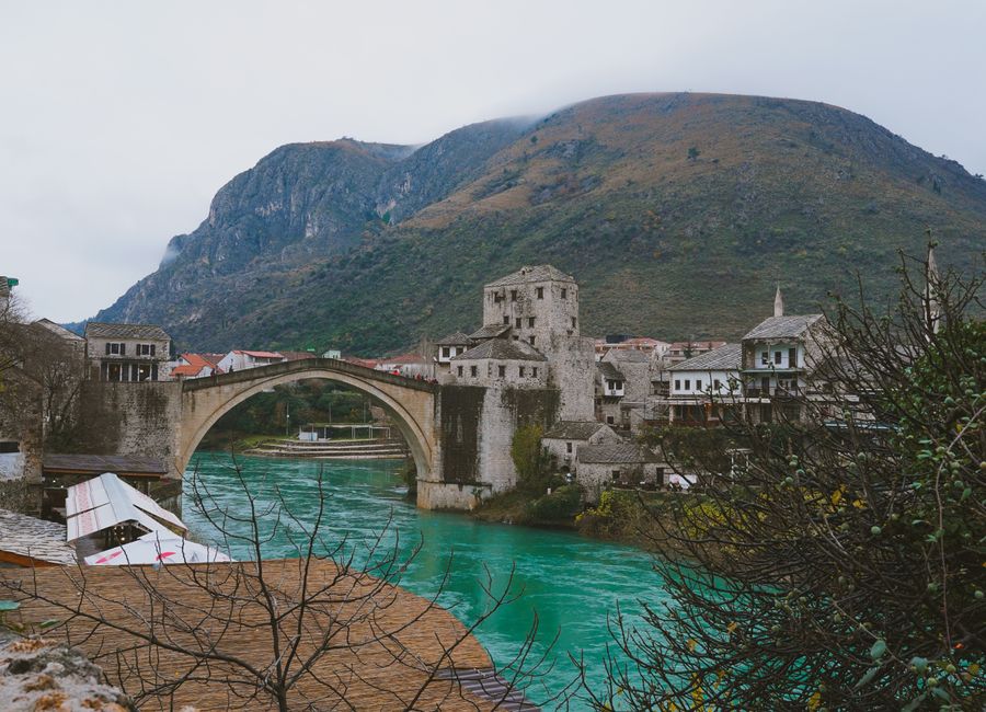 Scenic view of Mostar's famous Old Bridge over the emerald Neretva River, surrounded by historic buildings.