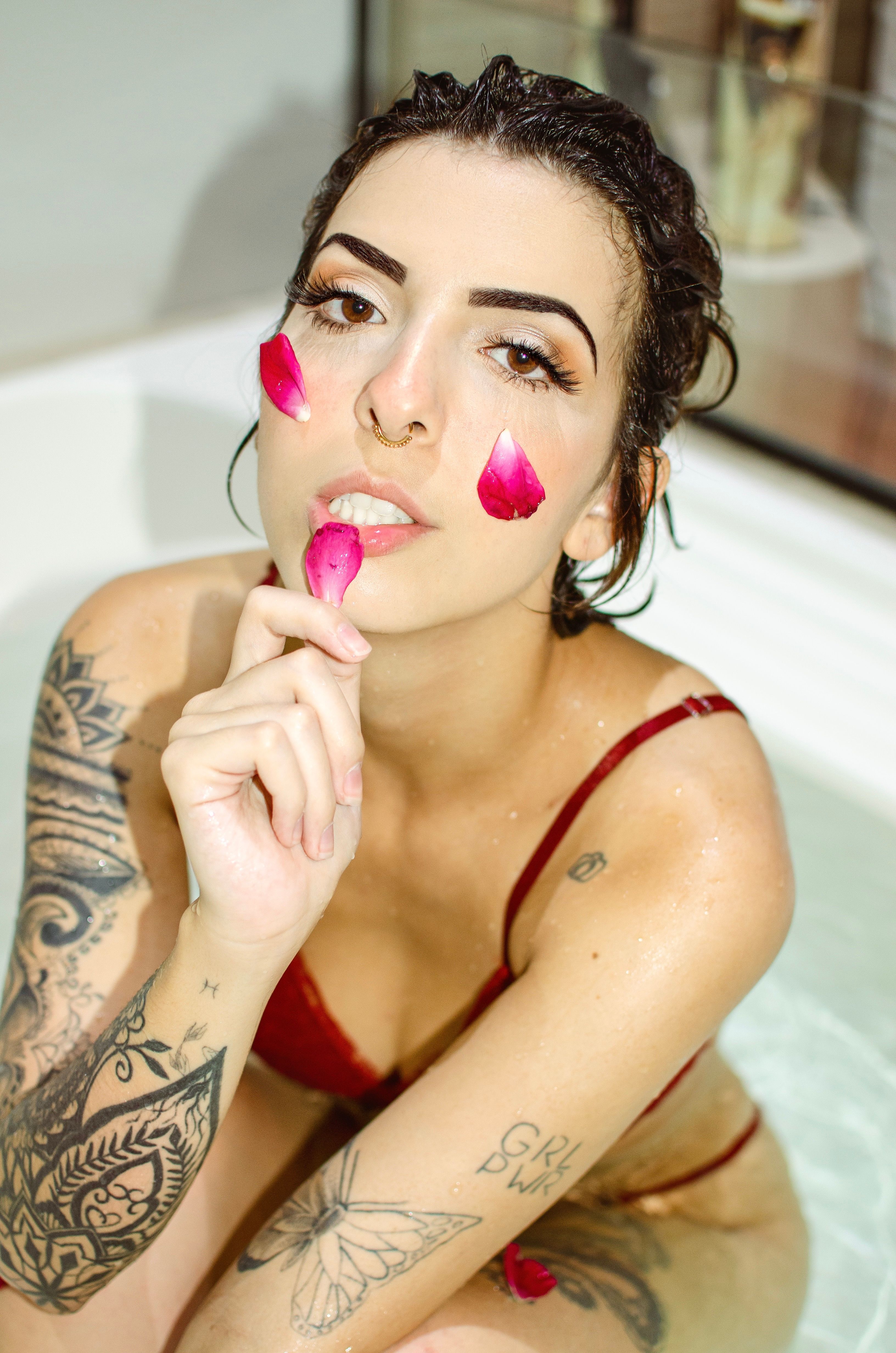 Artistic portrait of a woman with tattoos, sitting in a bathtub with rose petals.