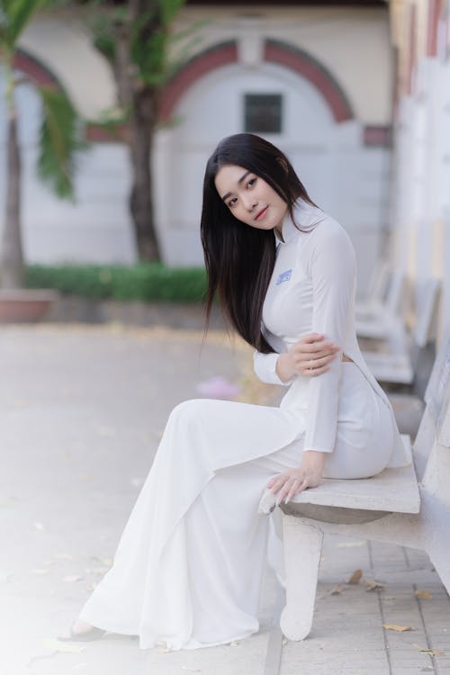 Young Woman in an Elegant White Dress Sitting on a Bench 