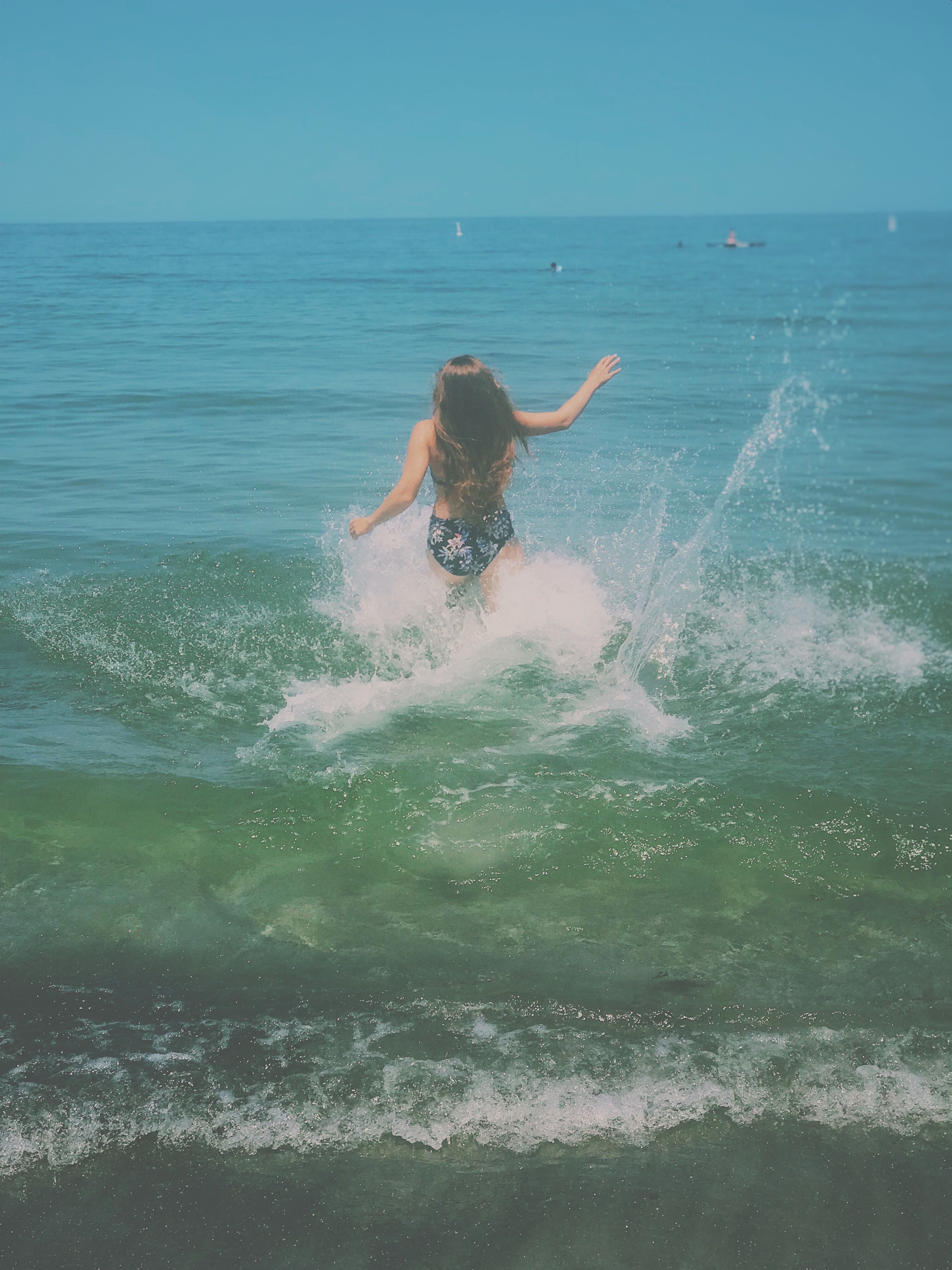 Back view of a woman with long hair splashing in ocean waves during summer vacation.