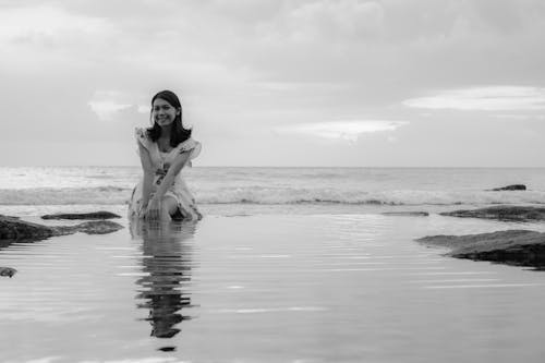 Smiling Woman in Sundress Sitting in Water on Sea Shore in Black and White