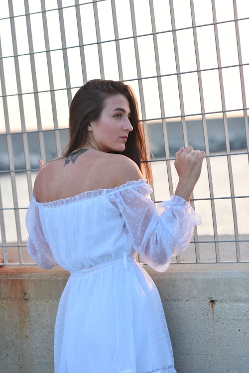 Young Woman in a White Dress Standing against a Fence 