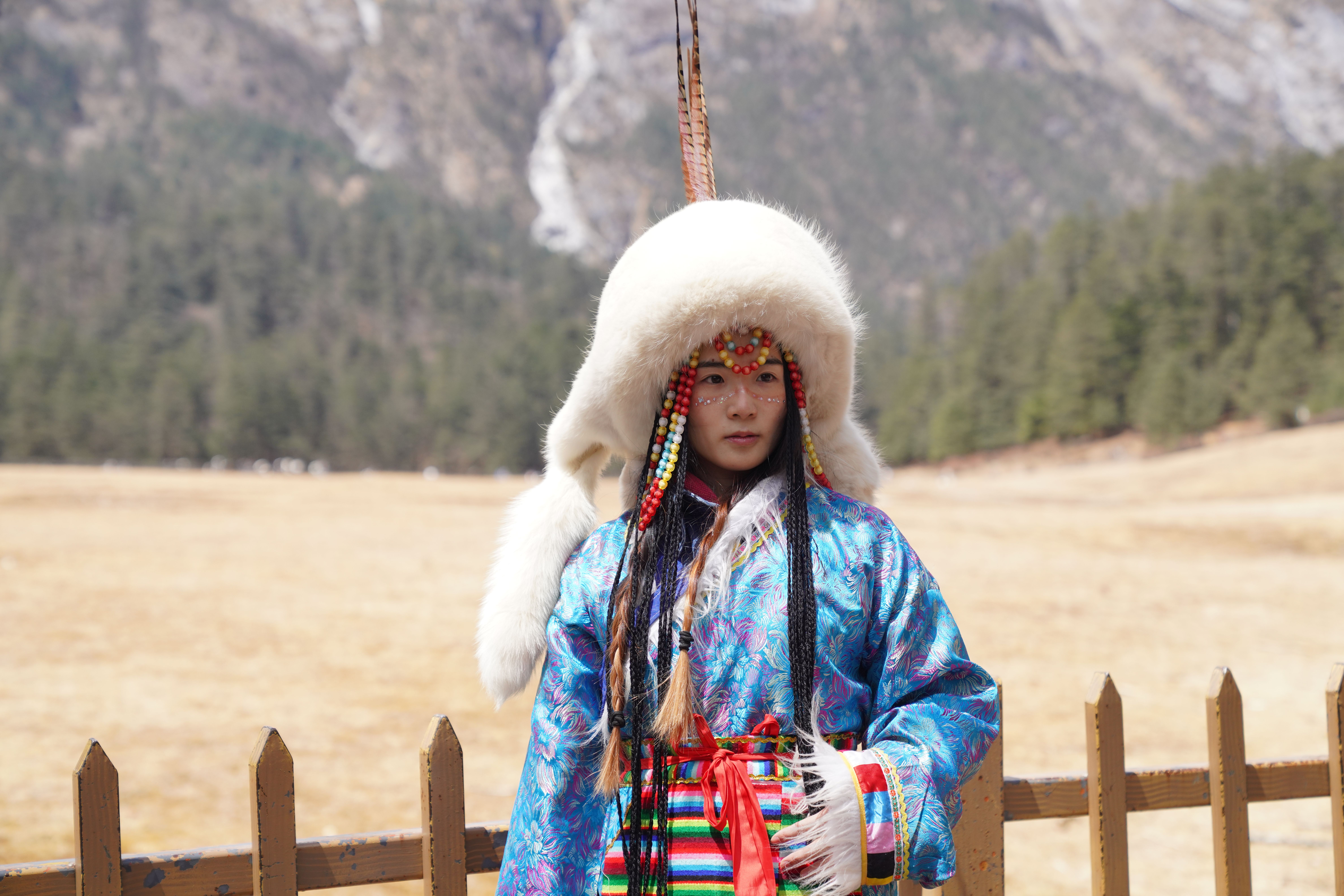 Portrait of a person in traditional Mongolian clothing against a mountainous backdrop.