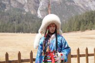 Portrait of a person in traditional Mongolian clothing against a mountainous backdrop.