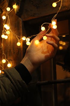 A hand holding glowing string lights against a wooden background, creating a warm atmosphere.