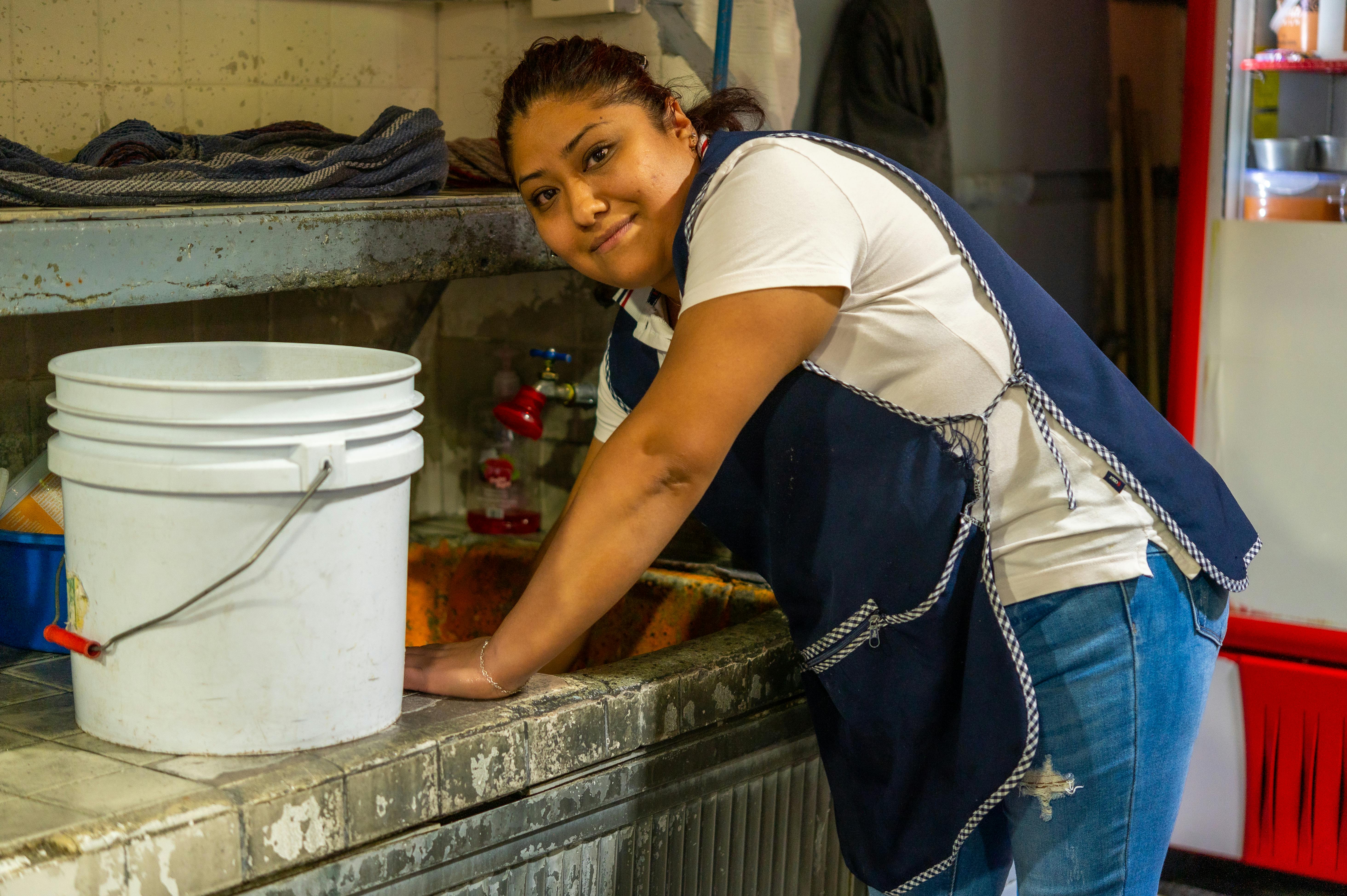 A woman in an apron is washing a bucket