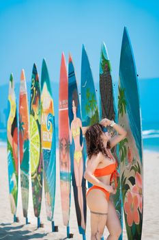 A woman in a bikini poses by artistic surfboards by the ocean, capturing a vibrant beach scene.