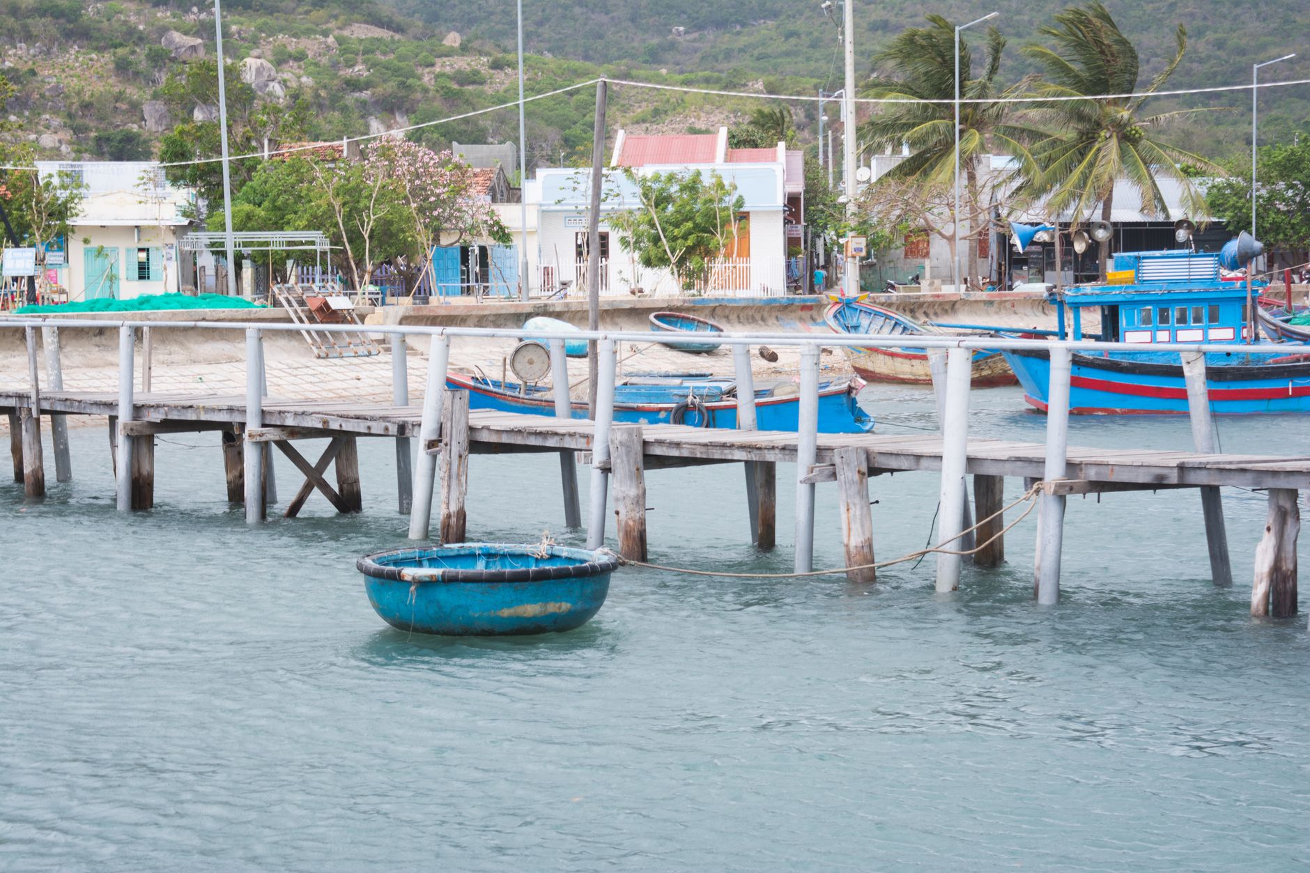Charming pier in Ninh Thuận, Vietnam with colorful fishing boats and lush surroundings.