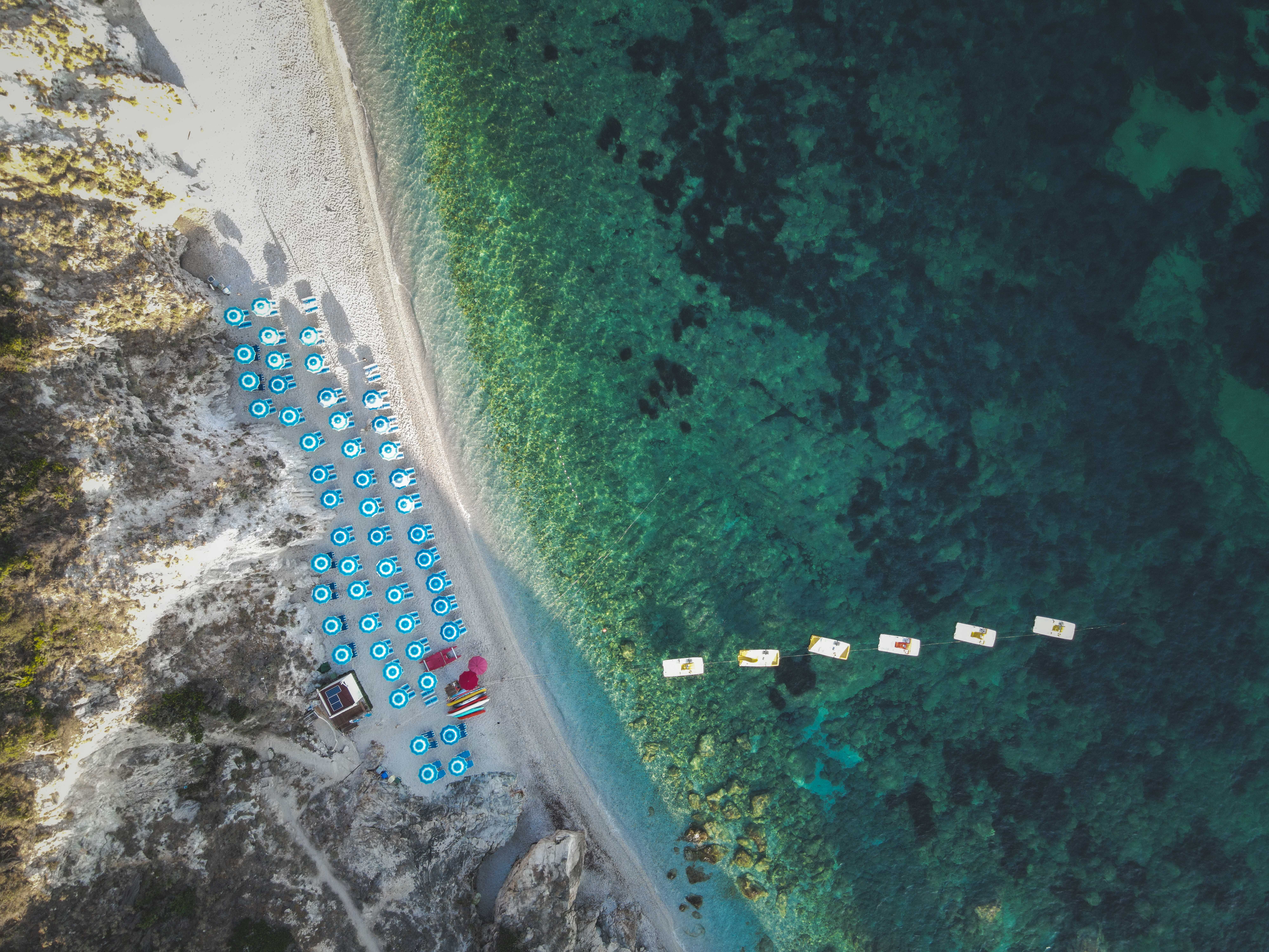 Stunning aerial beach view with blue umbrellas and clear turquoise waters.