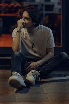Thoughtful young man sitting casually on a sidewalk in Fethiye, Türkiye, at night.