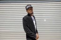 一名自信的男子头戴黑色帽子、身穿夹克，在户外金属背景前摆出姿势