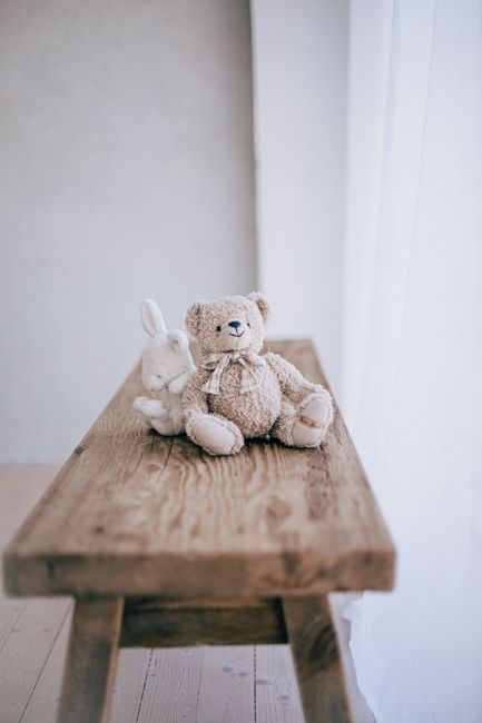 Teddy bear and rabbit plush toys sit on a rustic wooden table, creating a cozy atmosphere.
