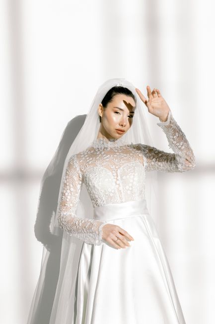 Stunning bride posing gracefully in an intricately designed lace wedding dress under soft sunlight.