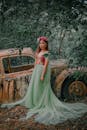 一名身穿绿色连衣裙的女子在郁郁葱葱的森林中，优雅地倚靠着一辆旧车摆姿势