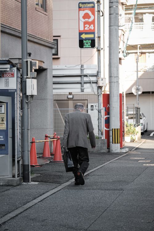 Free A man walks away in an urban street with orange cones and signage visible, depicting city life. Stock Photo