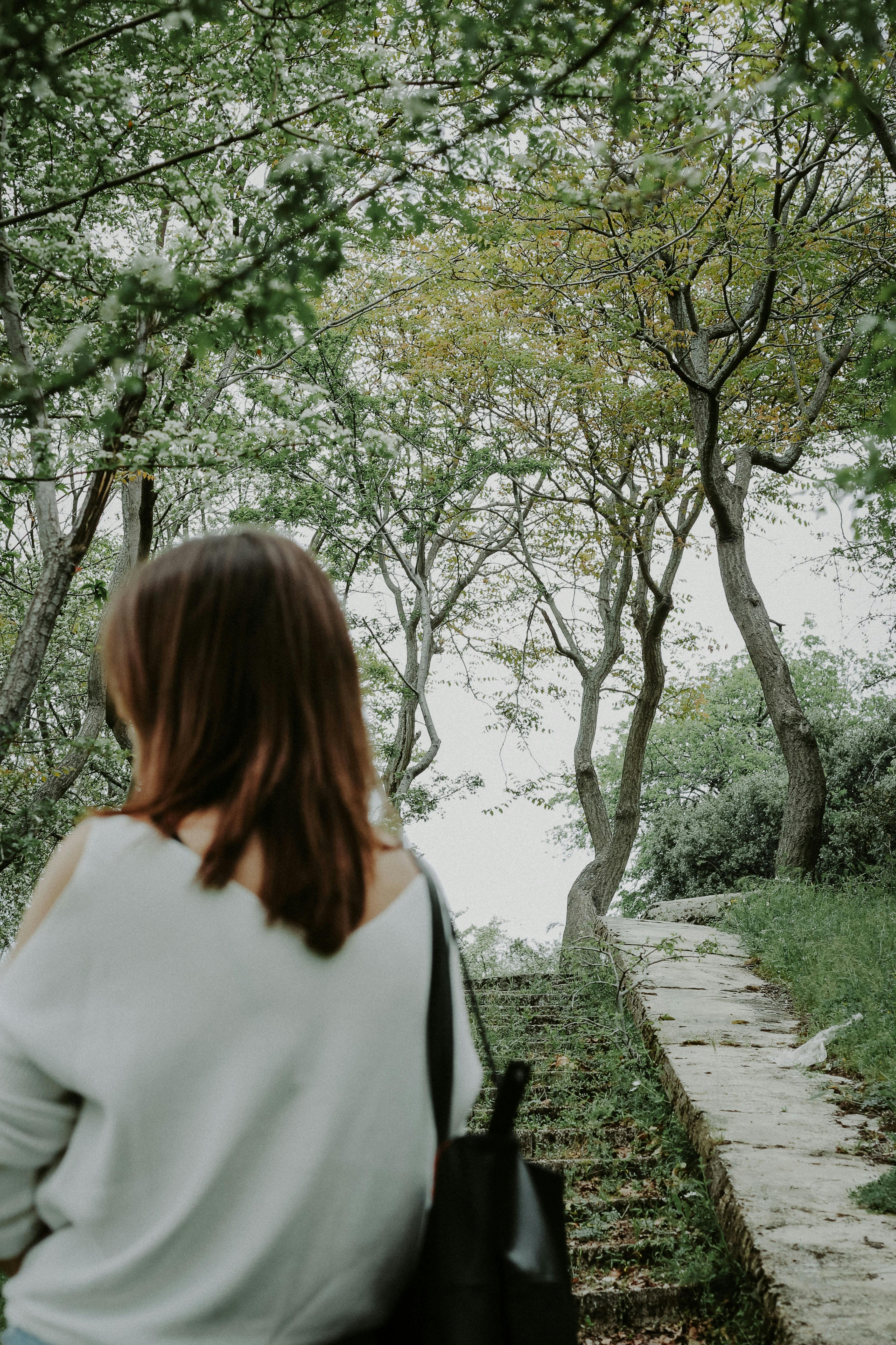 Woman exploring tranquil park path surrounded by lush green trees and nature.