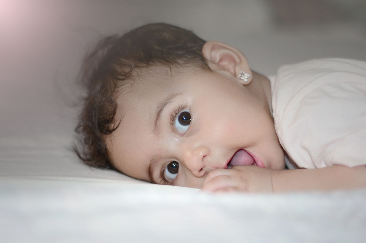 charming baby girl with big brown eyes lying on bed showing innocence