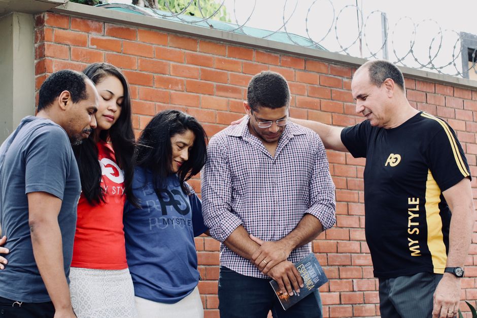 A diverse group of adults praying together, eyes closed in focus and unity.