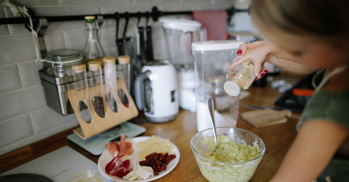 Close up of a hand massaging salt into shredded cabbage in a glass bowl