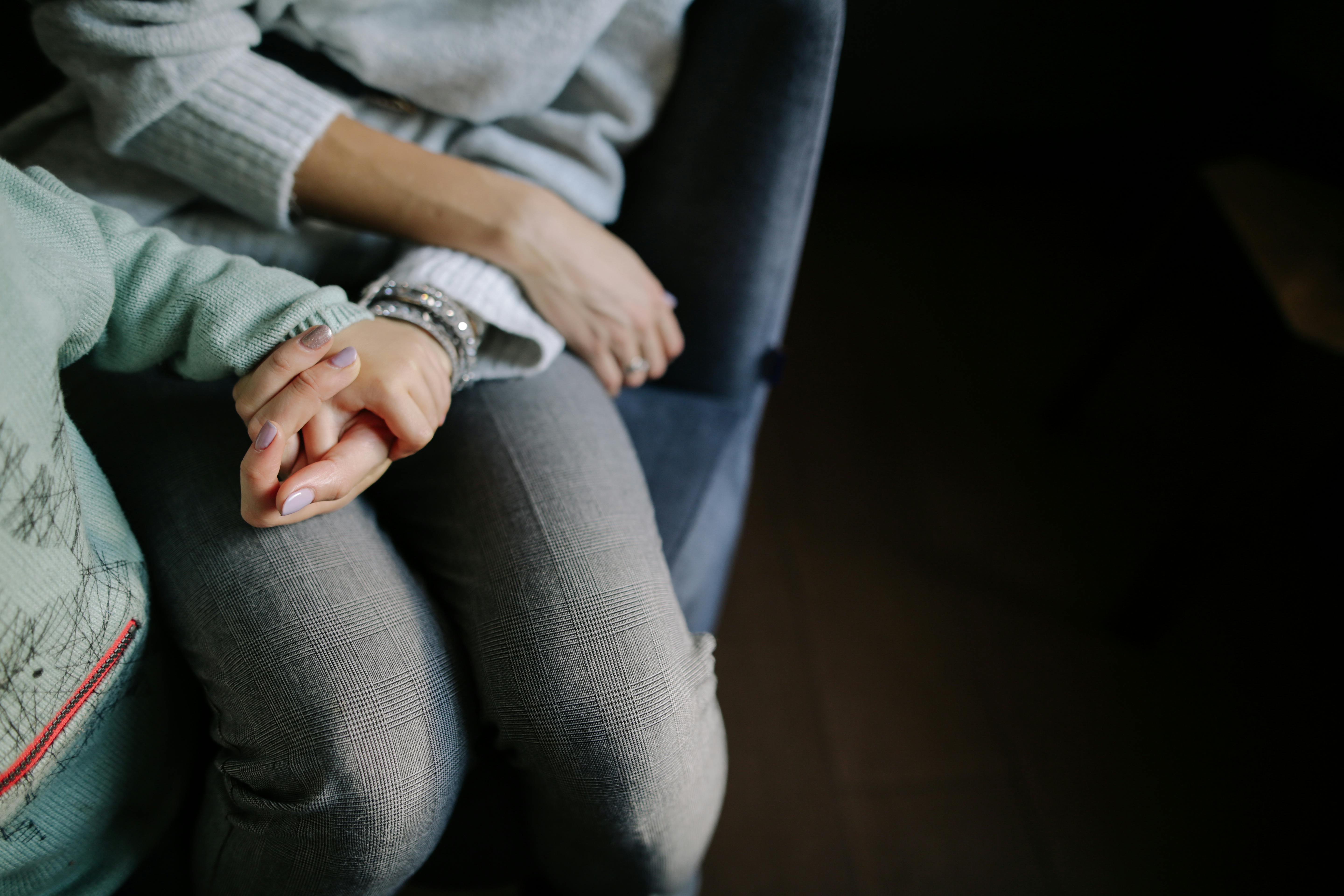 sitting woman in gray long sleeved shirt holding baby s hand in blue long sleeved shirt