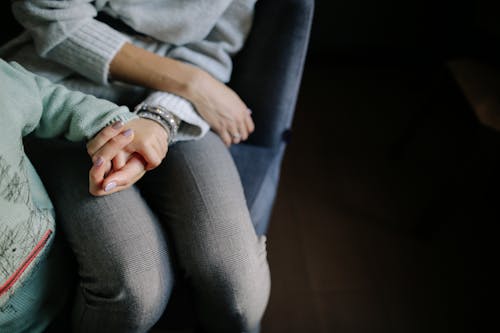 Donna Seduta In Camicia A Maniche Lunghe Grigia Che Tiene La Mano Del Bambino In Camicia A Maniche Lunghe Blu