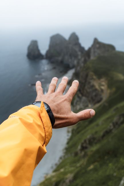 A hand extends toward dramatic cliffs on a Russian coast, perfect for adventure and travel themes.