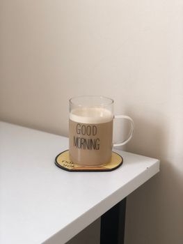 Clear glass mug with latte on a white table with 'Good Morning' text, creating a minimalist vibe.
