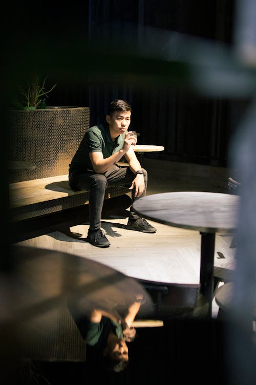 Young Man Sitting on a Bench in a Night Outdoor Cafe