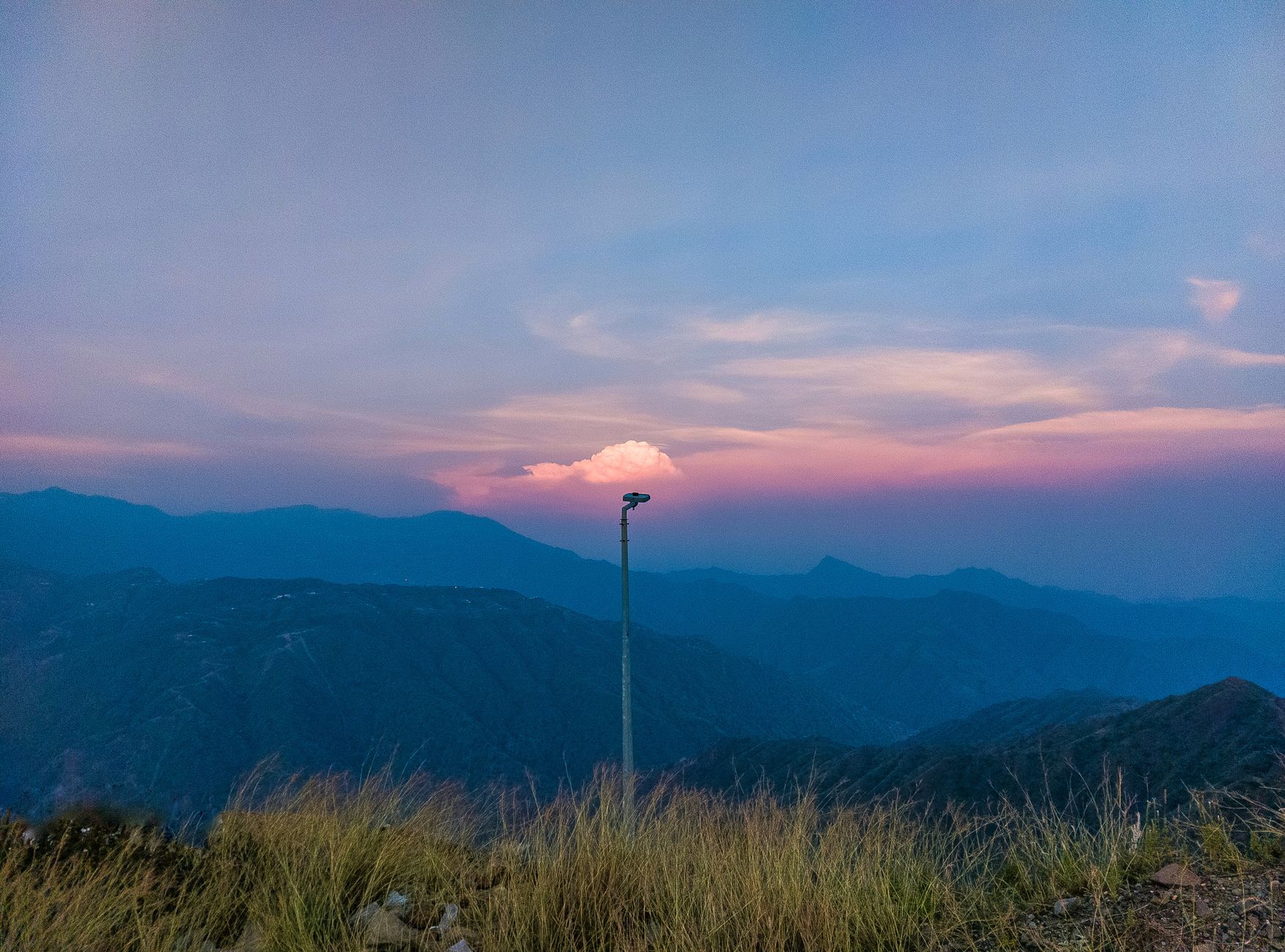 A tranquil sunset view with a lamp post against mountains and colorful sky.