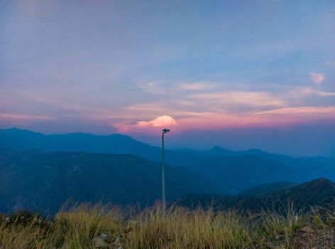 A tranquil sunset view with a lamp post against mountains and colorful sky.