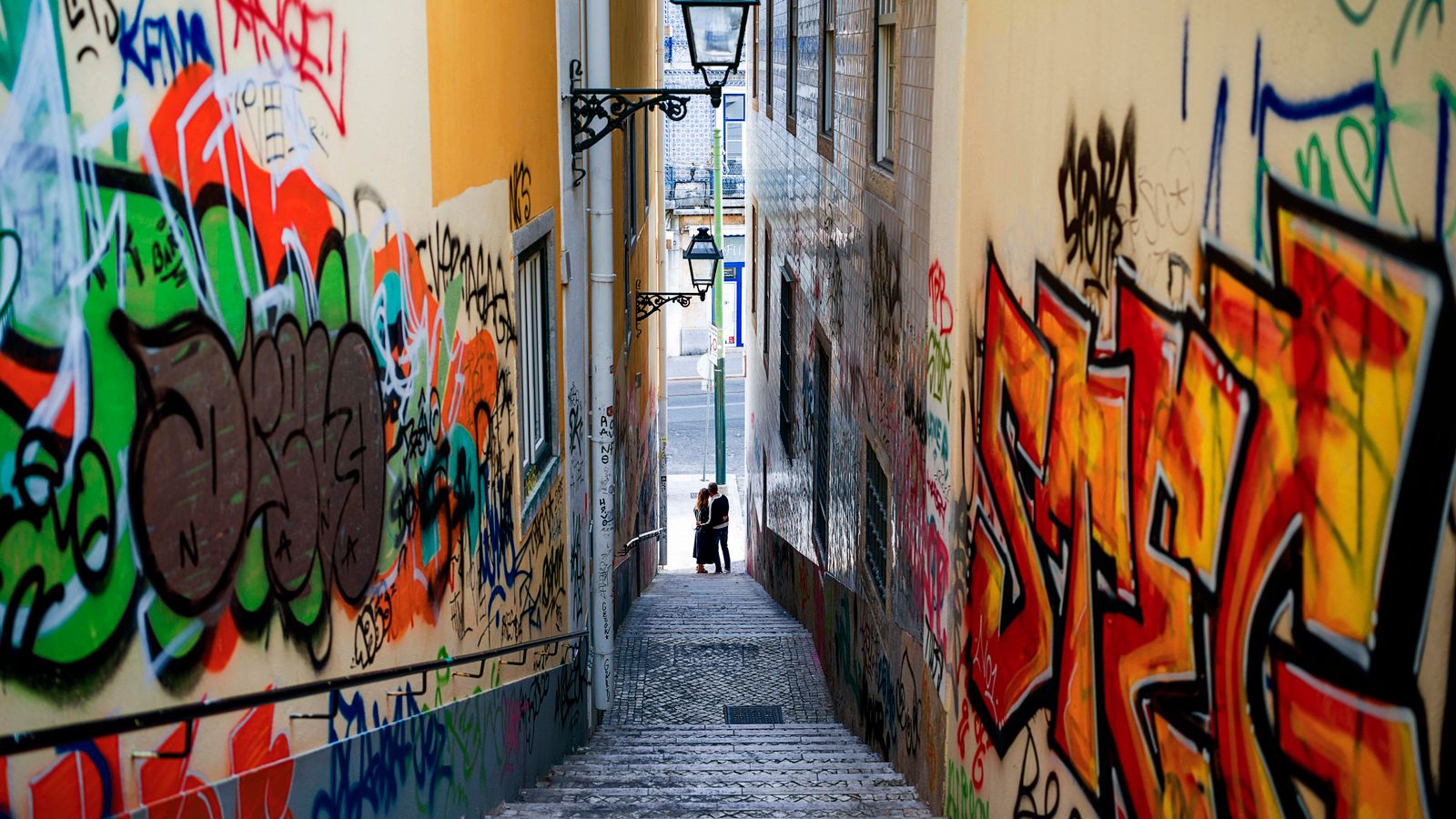Vibrant graffiti decorates a narrow alley in Lisbon, Portugal, offering a glimpse of urban art.