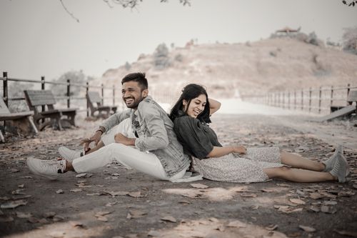 Free A happy couple sitting back-to-back on a leaf-covered path, laughing joyfully in autumn. Stock Photo