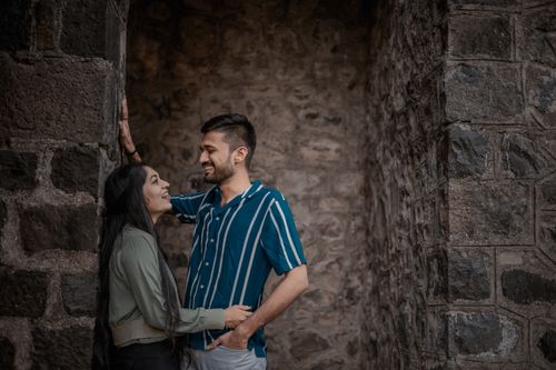 Free A joyful couple sharing a laugh while leaning on a rustic stone wall, capturing an intimate and playful moment outdoors. Stock Photo