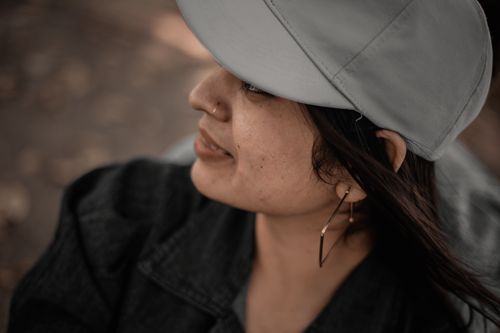 Free Close-up of a woman wearing a gray cap and geometric earring outdoors. Stock Photo