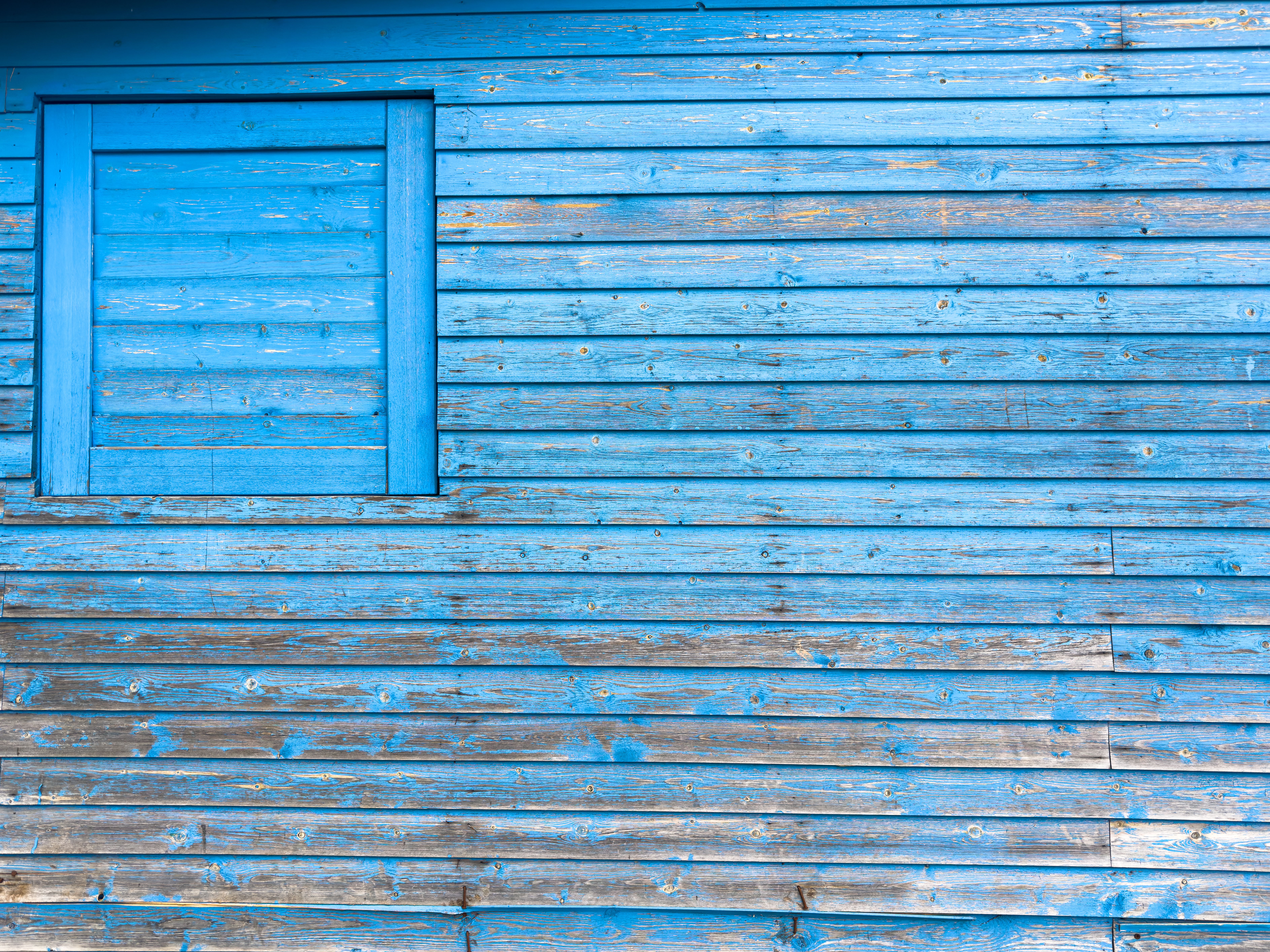 Blue weathered wooden wall with a small blue-framed window on the left