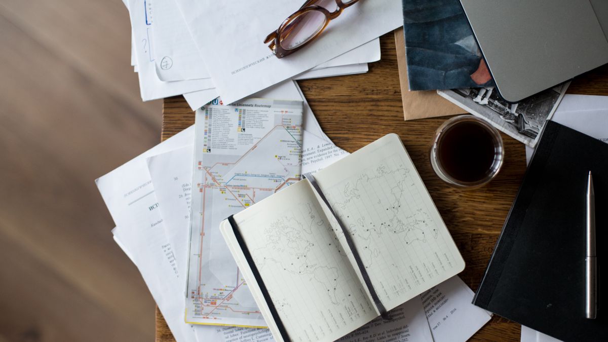 Flat lay of a workspace with coffee, maps, laptop, and documents on a wooden desk.
