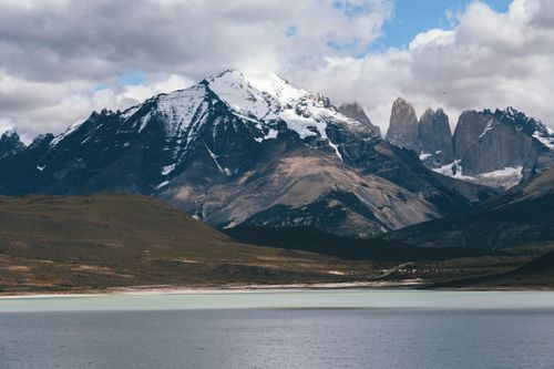 Free Explore the serene lake view of Torres del Paine's snow-capped mountains under a cloudy sky. Stock Photo