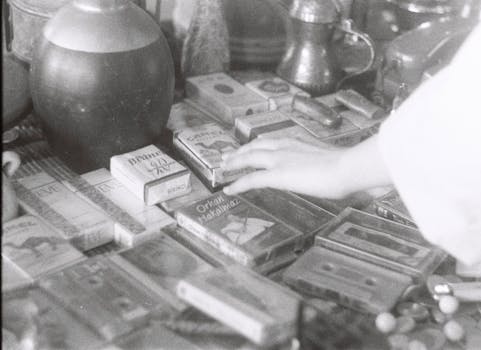Close-up of assorted vintage items, including tapes and cigarettes, on a flea market table in grayscale.