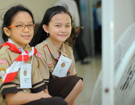 Two Asian girls in scout uniforms smiling indoors, in Jakarta, Indonesia.