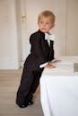 一个穿着燕尾服的可爱小男孩，自信地站在明亮的房间里