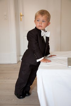 一个穿着燕尾服的可爱小男孩，自信地站在明亮的房间里