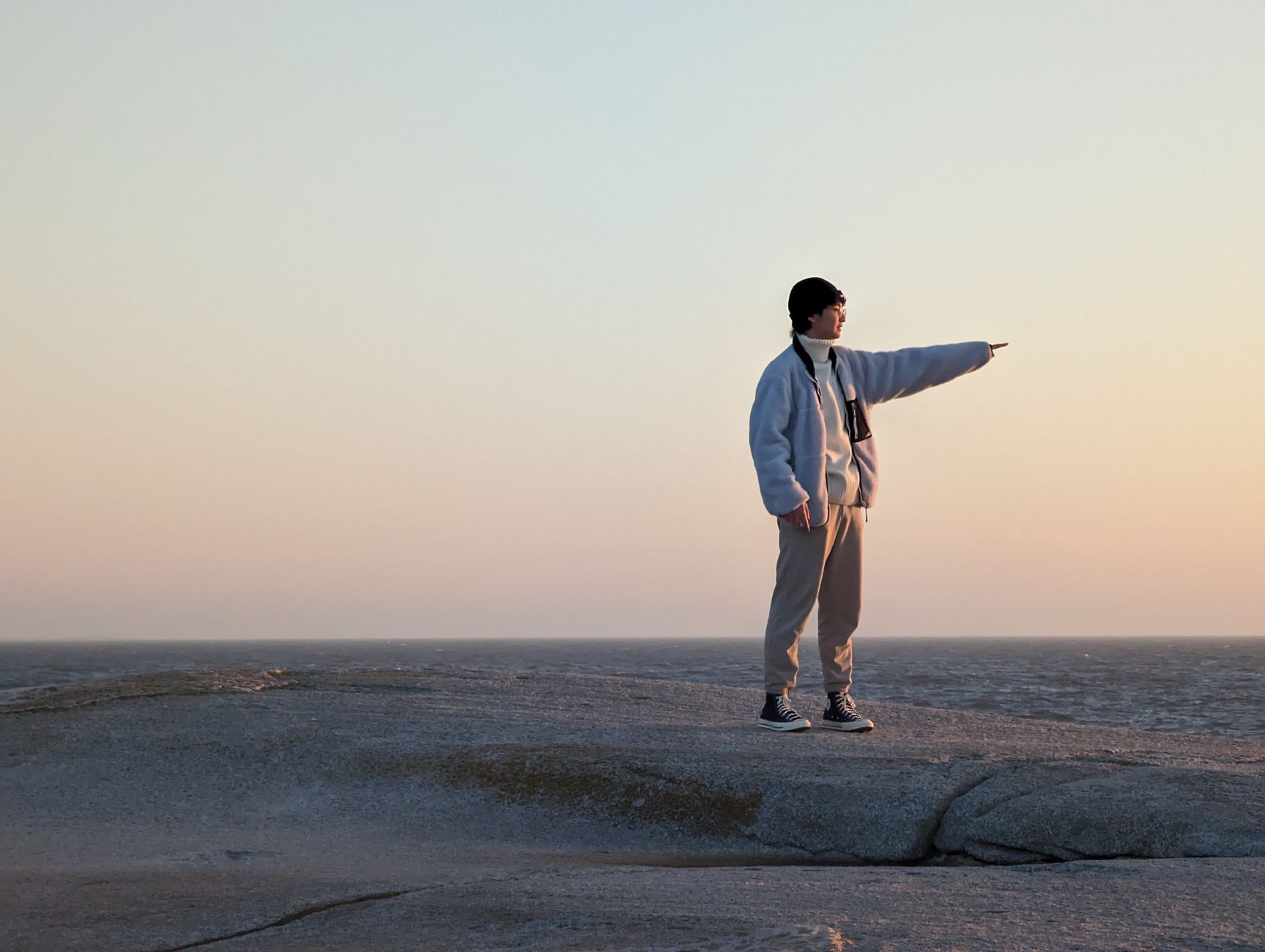 A person stands on rocky shore at Peggy's Cove, Nova Scotia during a beautiful sunset.