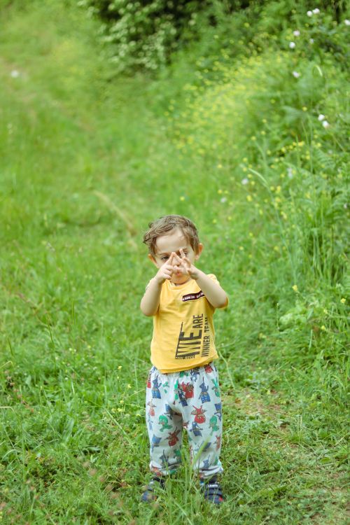 Free A small child gestures playfully in a lush green field, surrounded by nature. Stock Photo