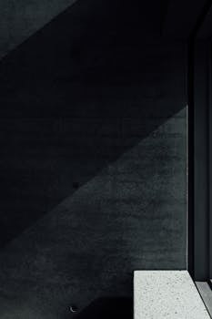 A striking minimalist photo featuring shadow play on a dark interior wall with a concrete surface.