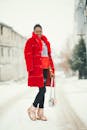 一位身穿鲜红色外套的时尚女士，走在白雪皑皑的街道上，展现了冬季的时尚