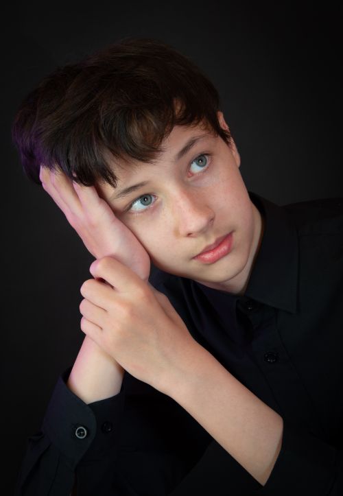 Free Portrait of a teenage boy leaning on hand against black background. Stock Photo