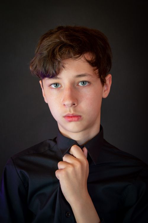Free Close-up portrait of a teenage boy in a black shirt against a dark background. Captivating and thoughtful. Stock Photo