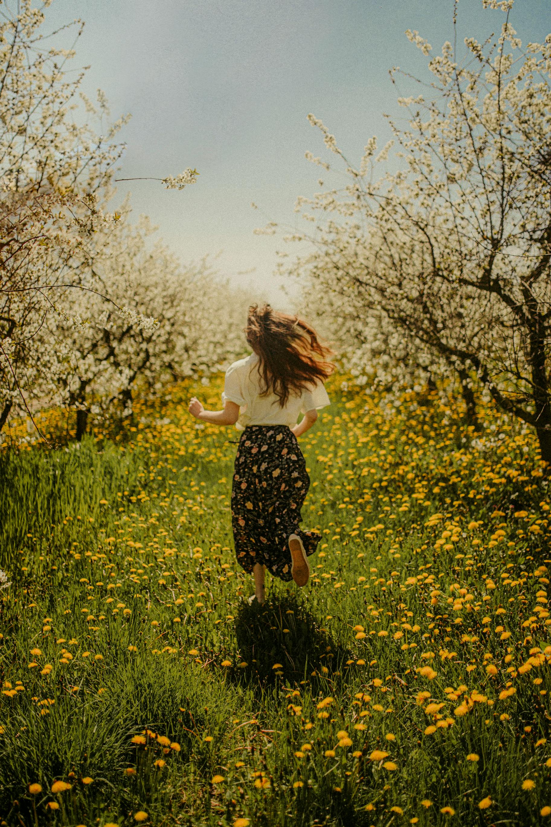 A carefree young woman runs through a meadow of blooming flowers and trees.
